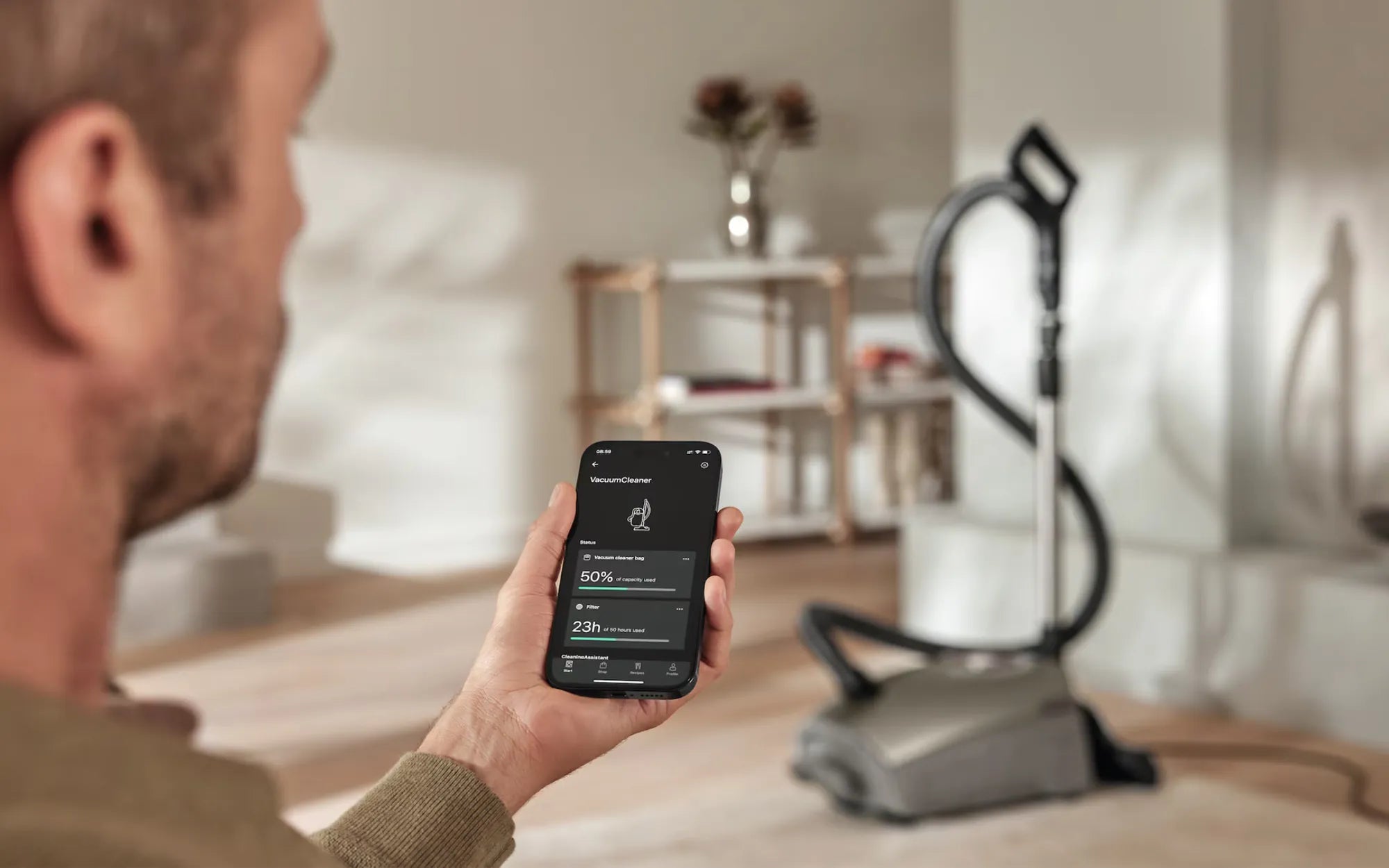 A man checking a vacuum's companion app next to his canister vacuum