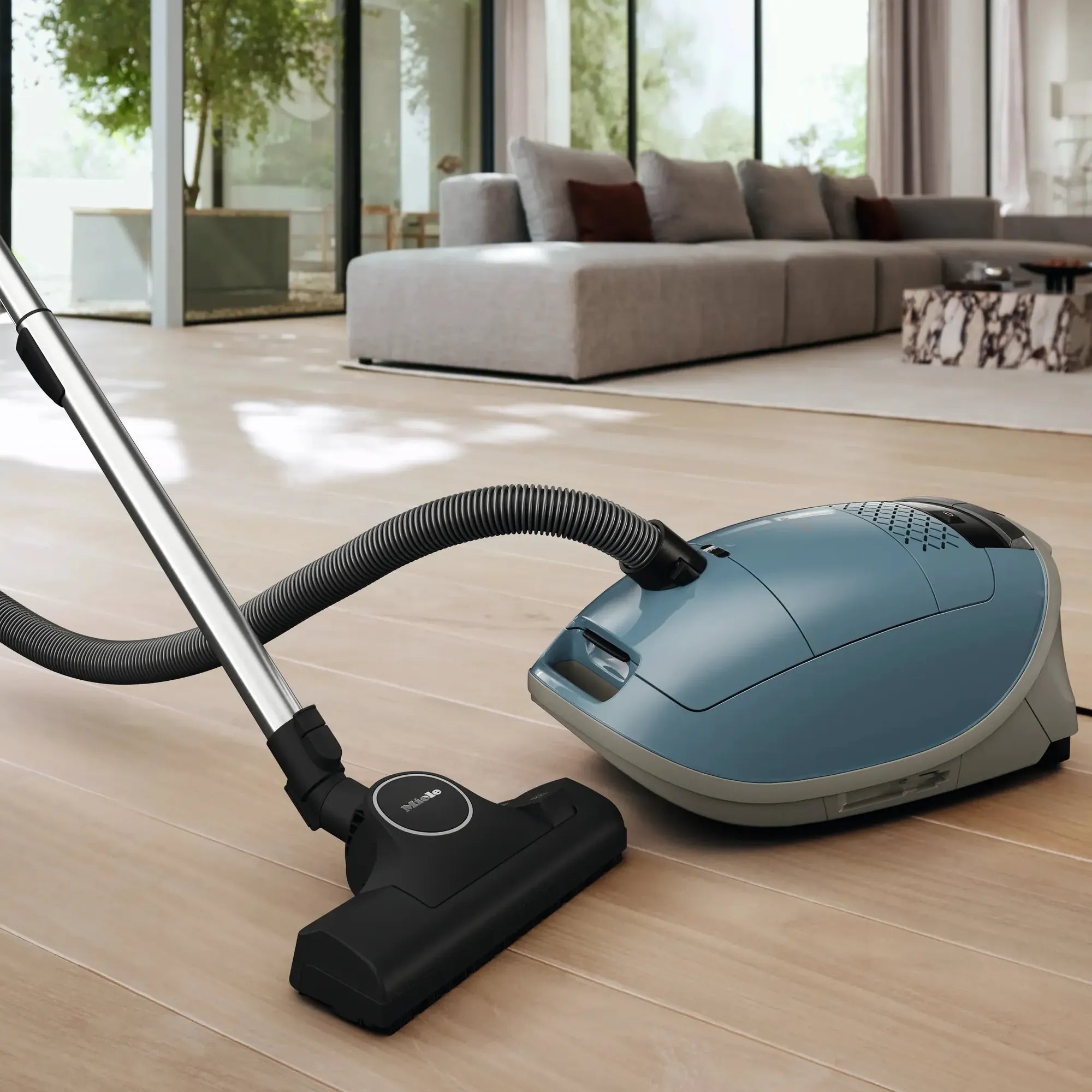 A blue canister vacuum with its hose and floor head on a wooden floor