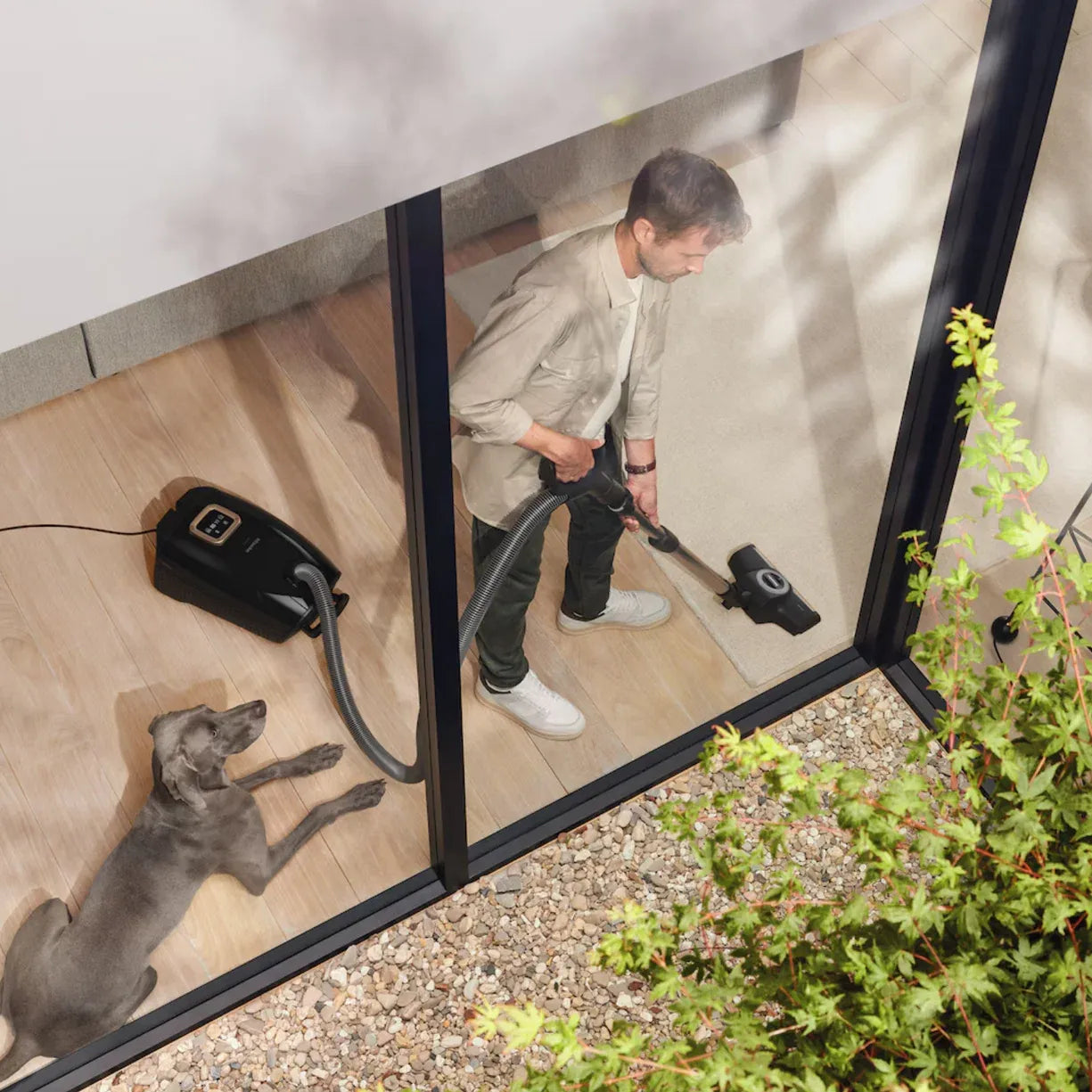 A man vacuuming a hallway floor, seen through a glass door