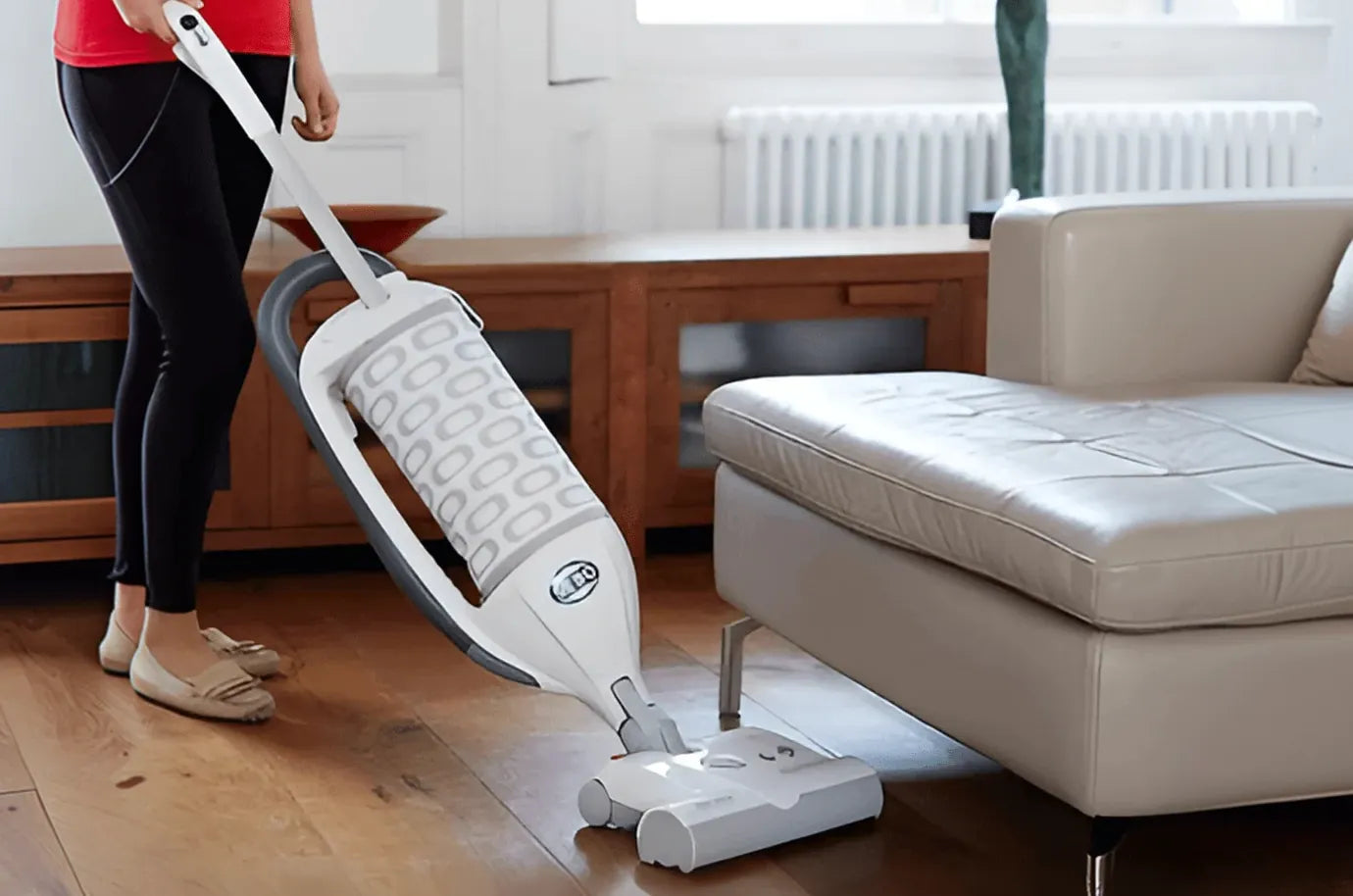 Someone vacuuming a wooden floor beside a sofa