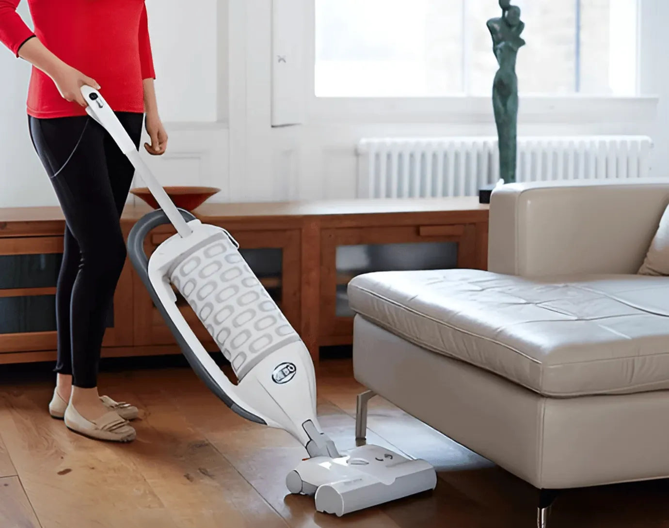 Someone vacuuming a wooden floor beside a sofa